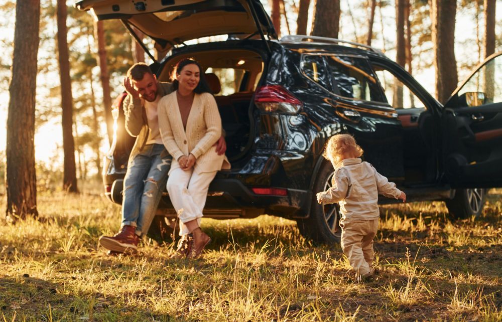 A family is sitting in the back of a car in the woods.