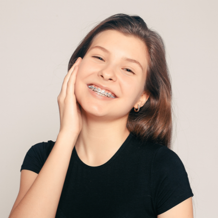 a young girl with braces on her teeth is smiling and touching her face .