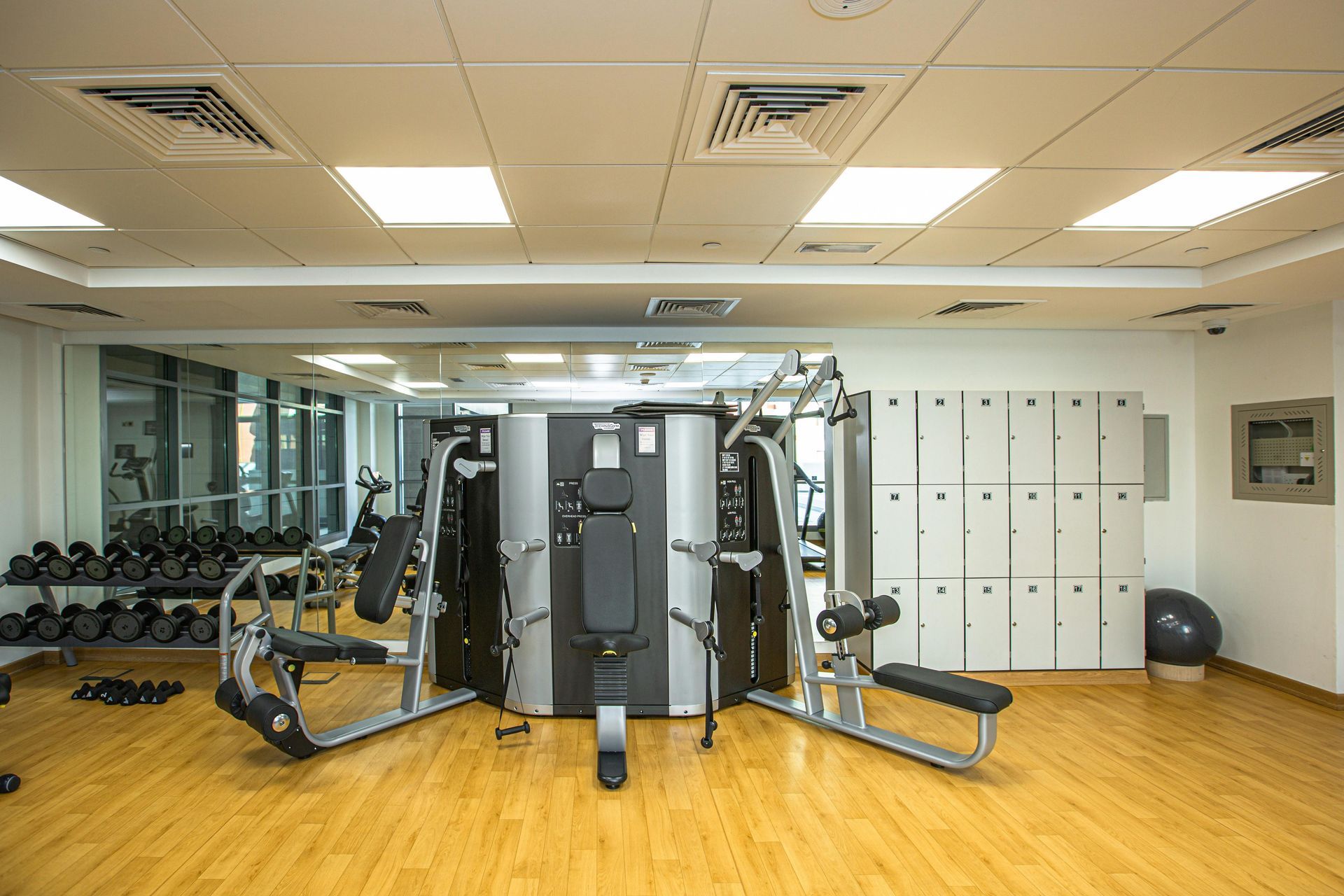 Gym with exercise machines, mirrors, lockers, and wood flooring