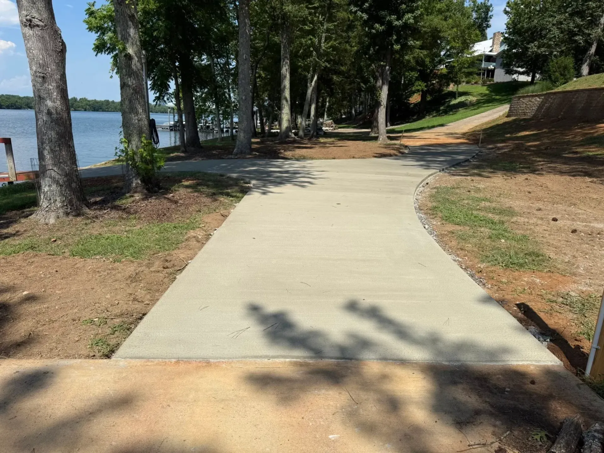 Concrete boat ramp curving toward a lake, lined with trees and grassy edges.