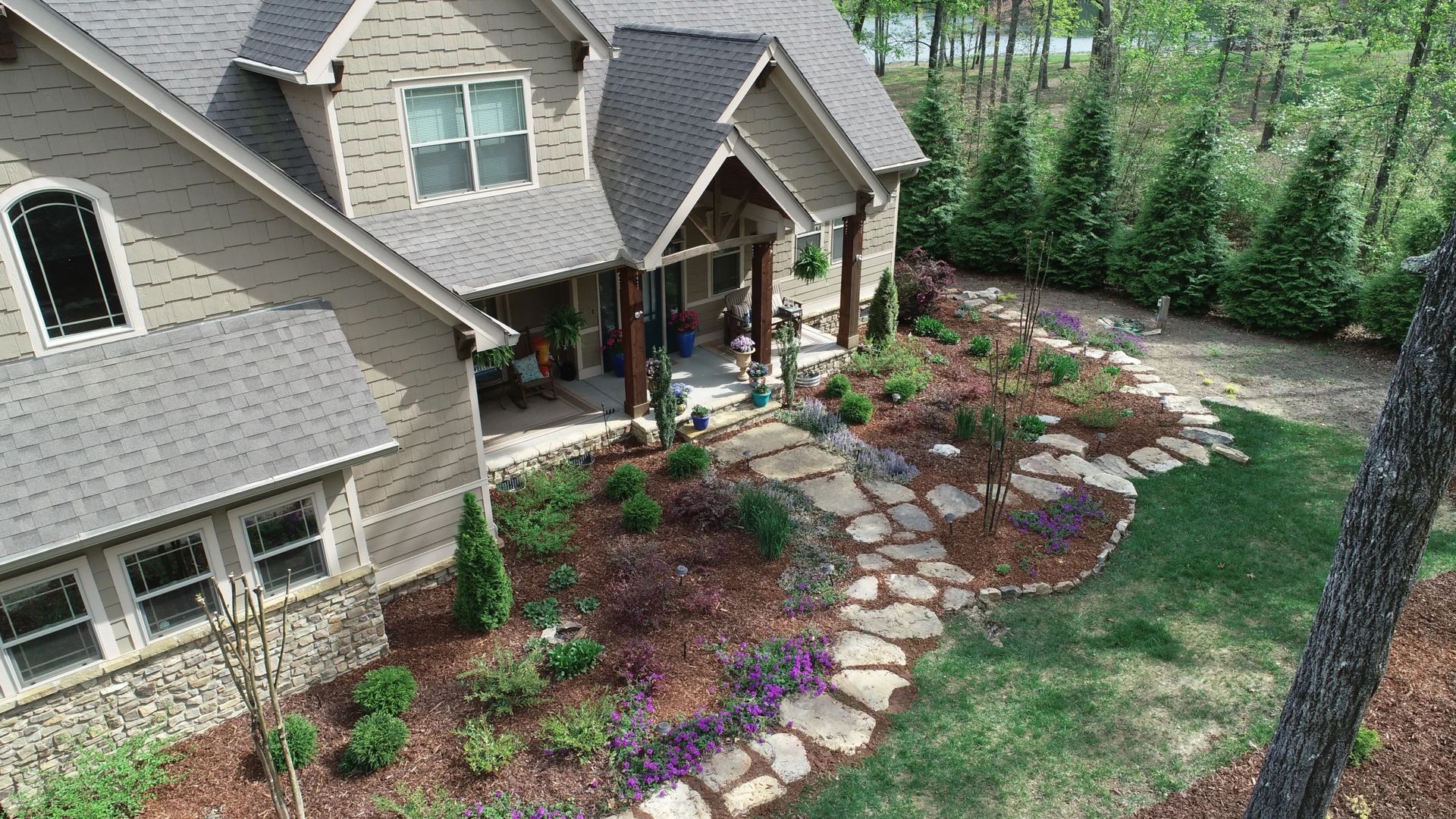 Stone path leads to a house with landscaping, bordered by trees and green lawn.