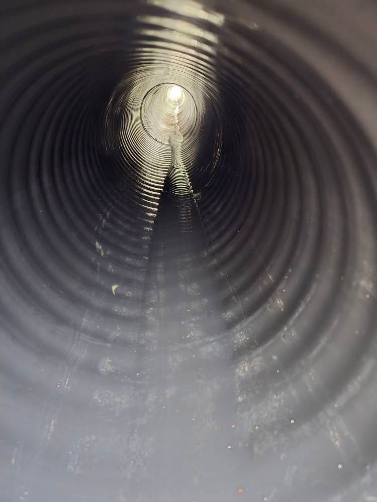 A view from inside a corrugated black plastic drainage pipe looking toward an opening with light at the end.