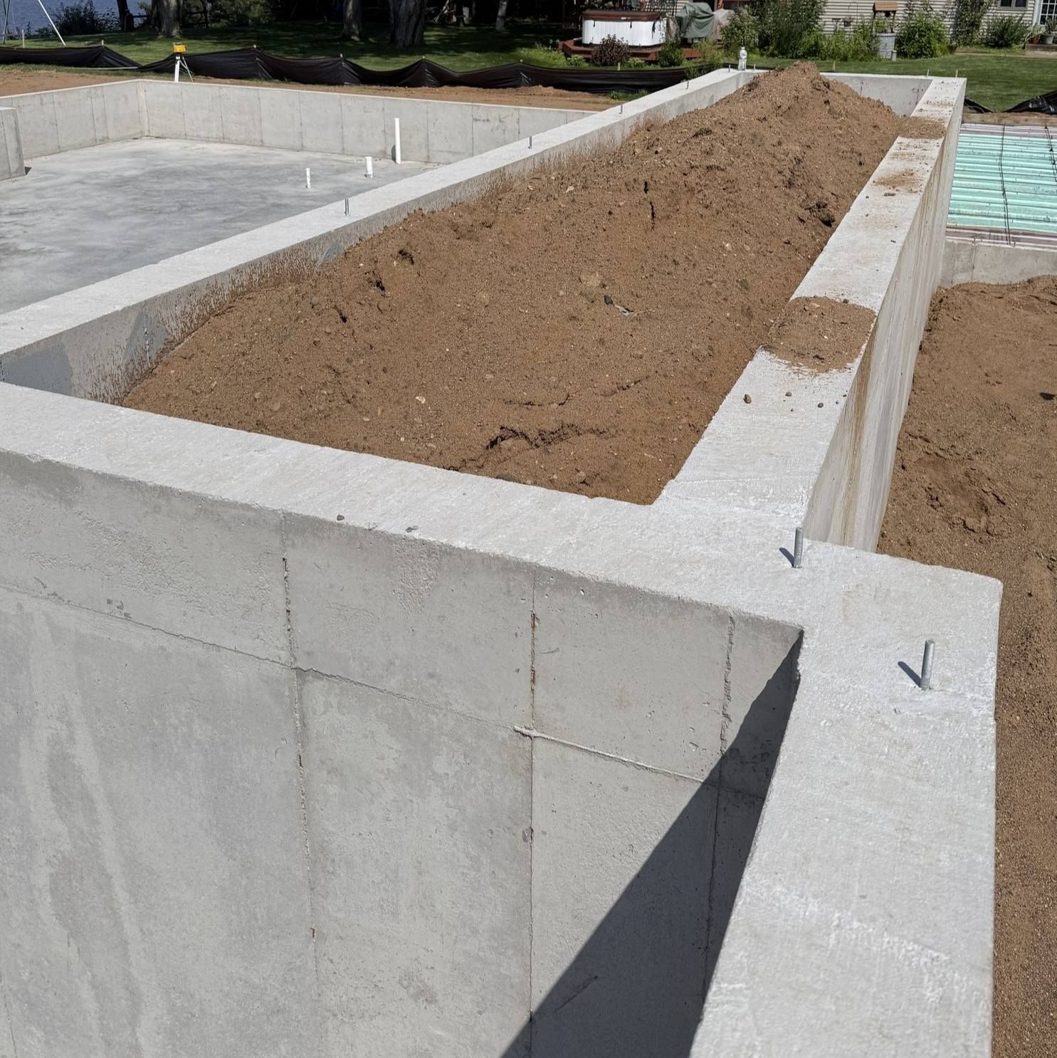 Concrete foundation walls filled with soil at an active residential construction site.