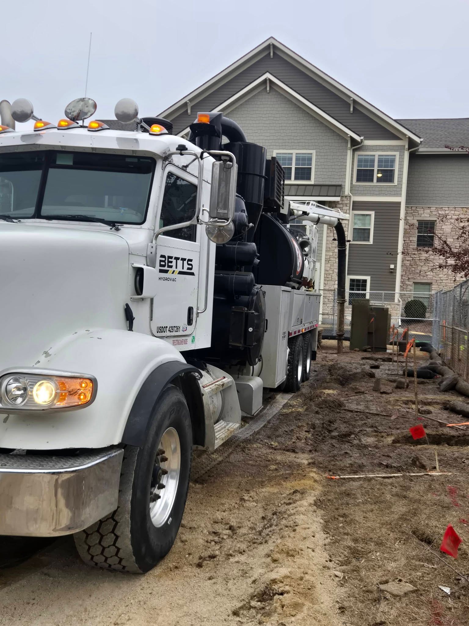 A white vacuum truck parked on a dirt construction site in front of a multi-story apartment building.