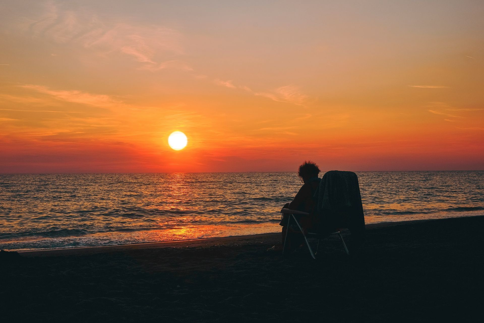 A person is sitting in a chair on the beach at sunset.