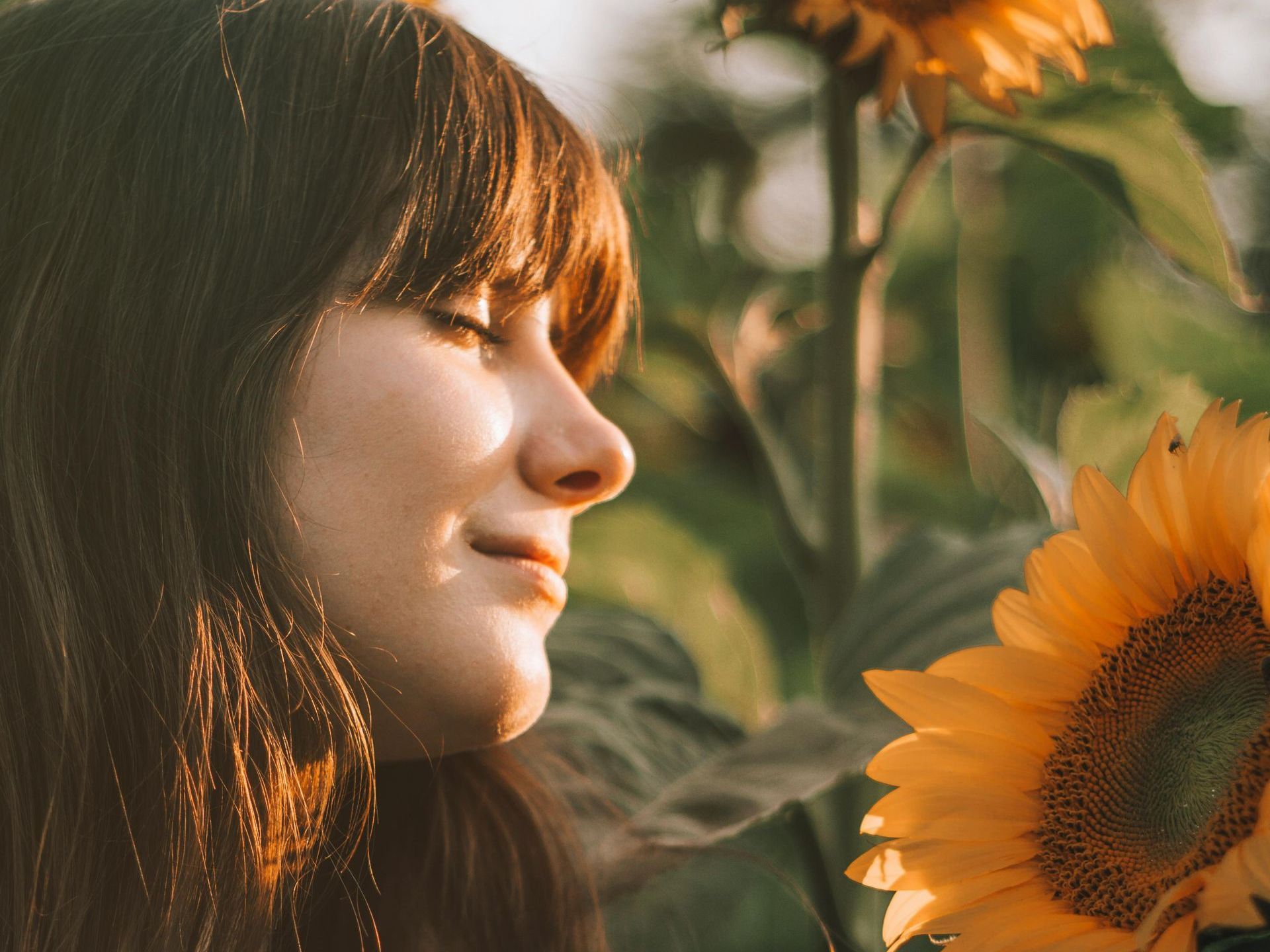 A woman is smelling a sunflower in a field.