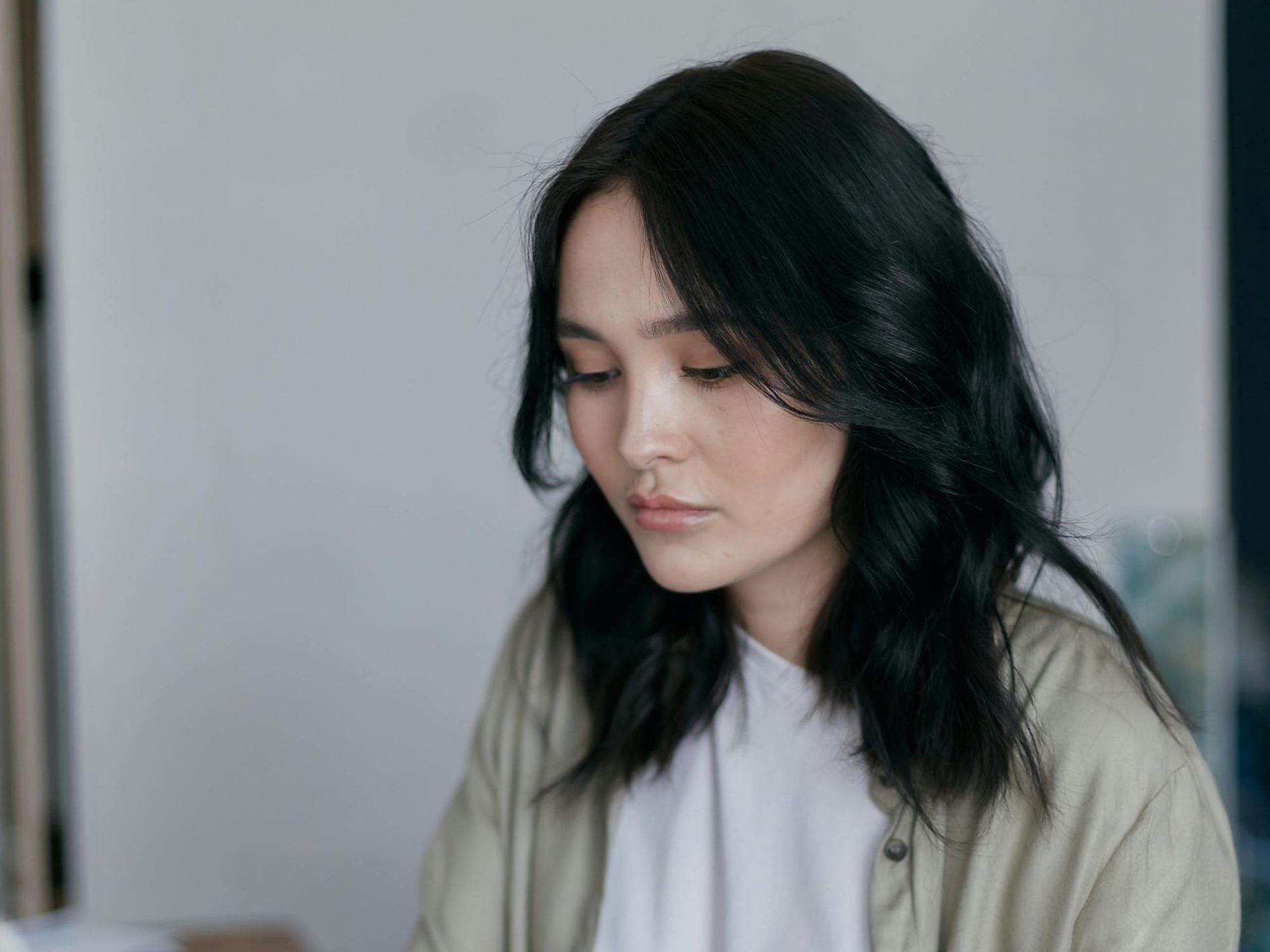 A woman with black hair is looking down at something while sitting at a table.