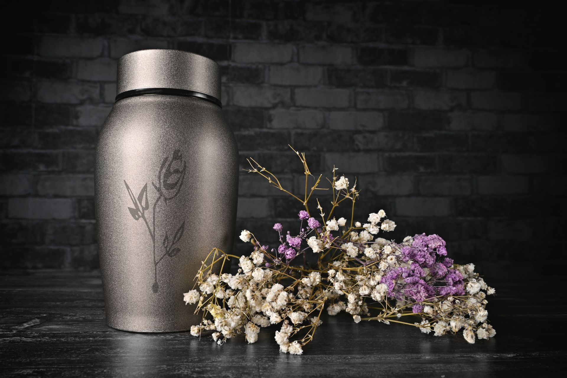 A urn with flowers on a table in front of a brick wall.