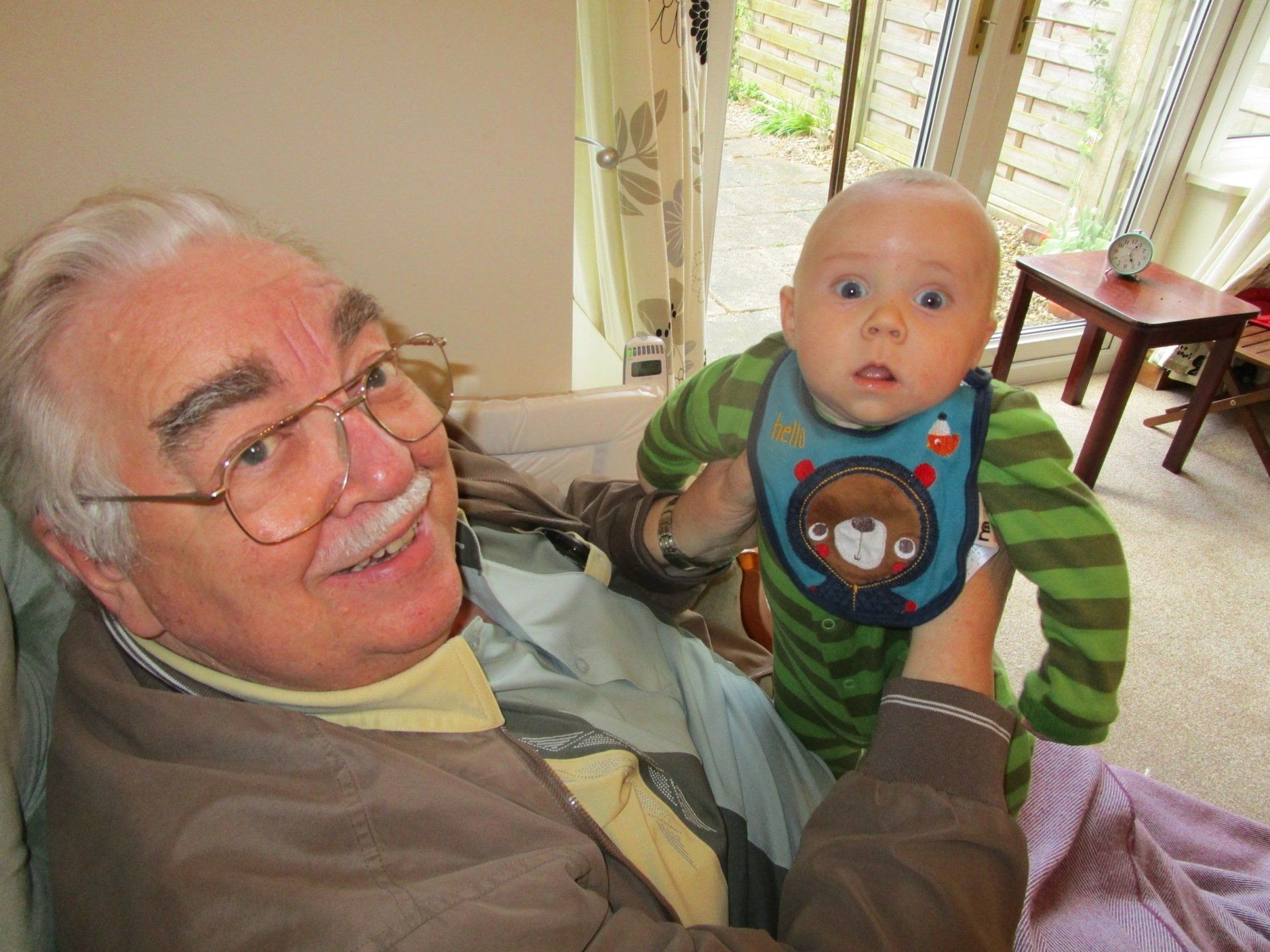 An elderly man is holding a baby in his arms.