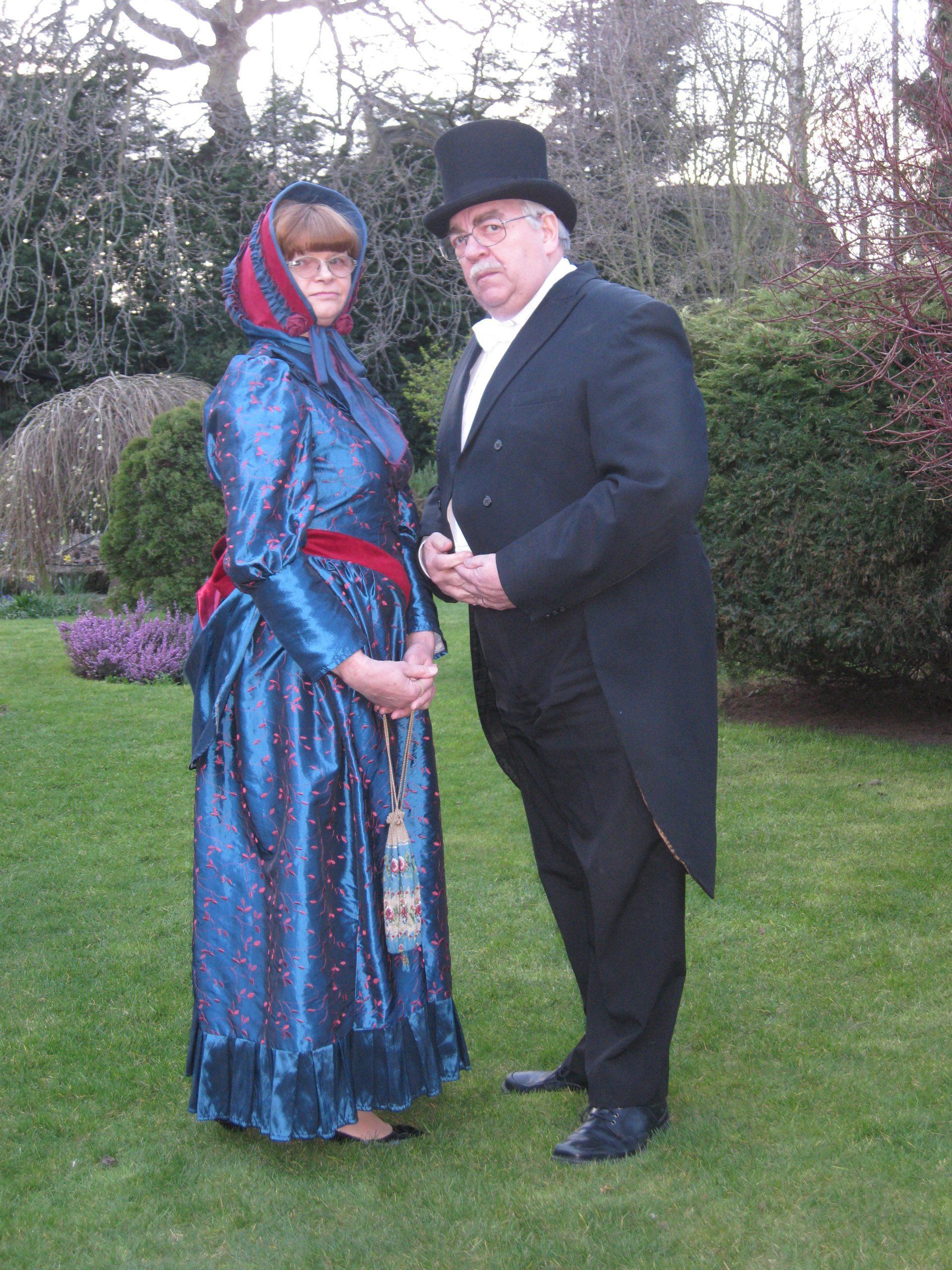 A man in a top hat stands next to a woman in a blue dress