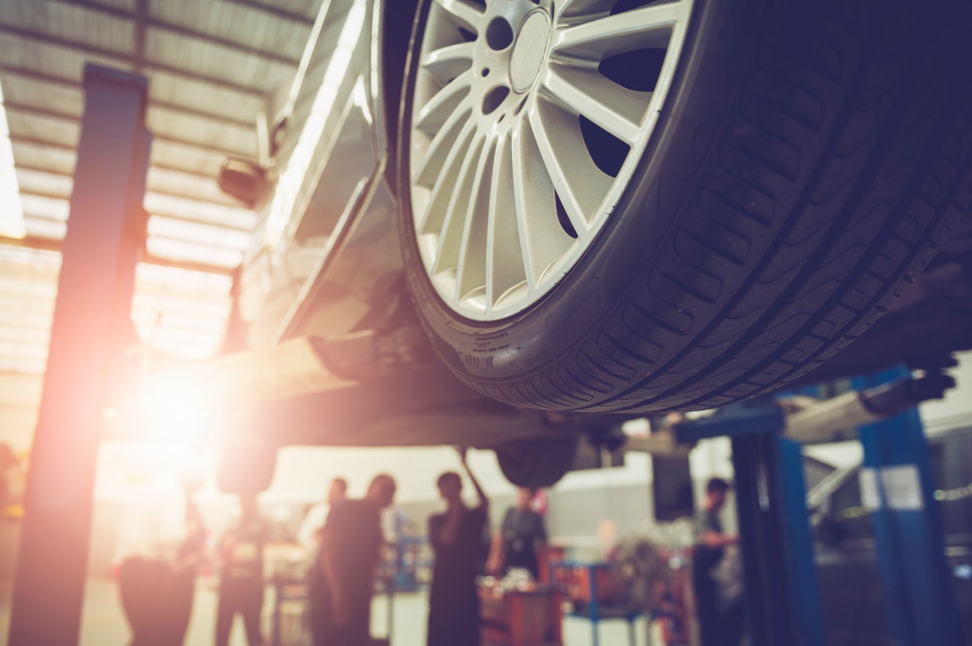 Car raised on a lift in a repair shop, mechanics working underneath.
