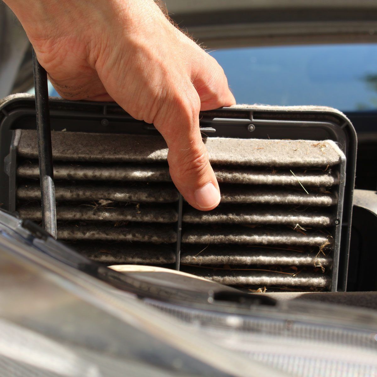 Hand removing a dirty car air filter from a compartment in the engine bay.