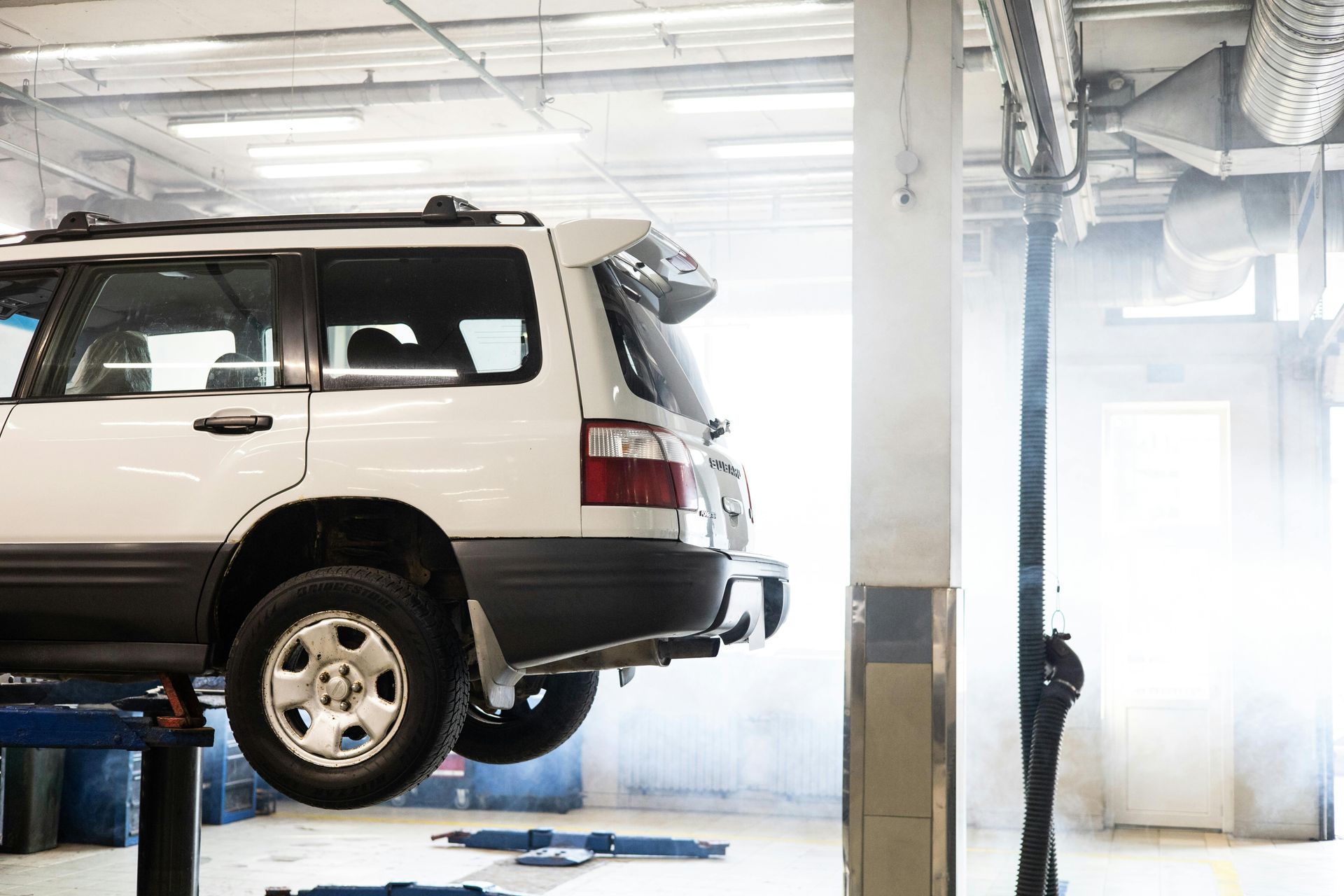 White SUV on a lift in a garage. Interior shot with visible exhaust system and support beams.