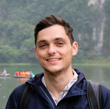 Smiling person outdoors by a lake with misty cliffs in the background