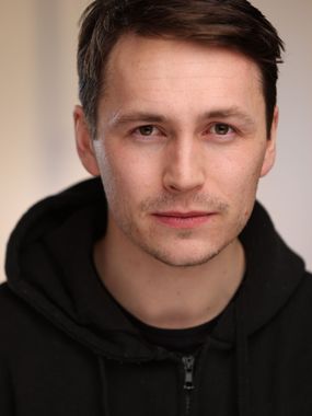 Close-up portrait of a person in a black hoodie with a neutral expression against a soft beige background