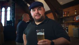 Man in a black cap and shirt holding a beer in a dimly lit bar.