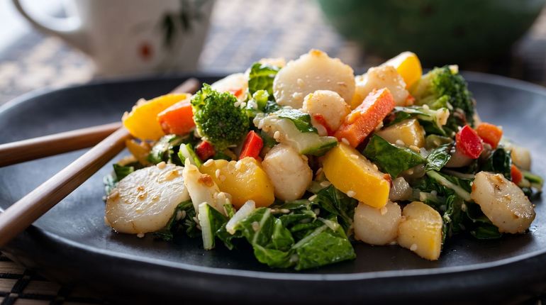 Colorful vegetable and grain salad on a black plate with chopsticks beside it