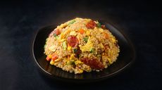 Plate of fried rice with diced meat and vegetables on a black dish