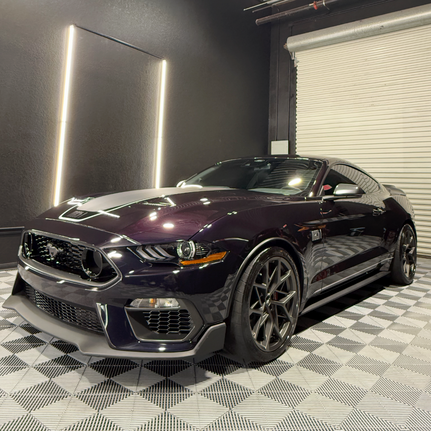 Dark purple sports car parked indoors on a checkered floor, shown from the front-left angle.
