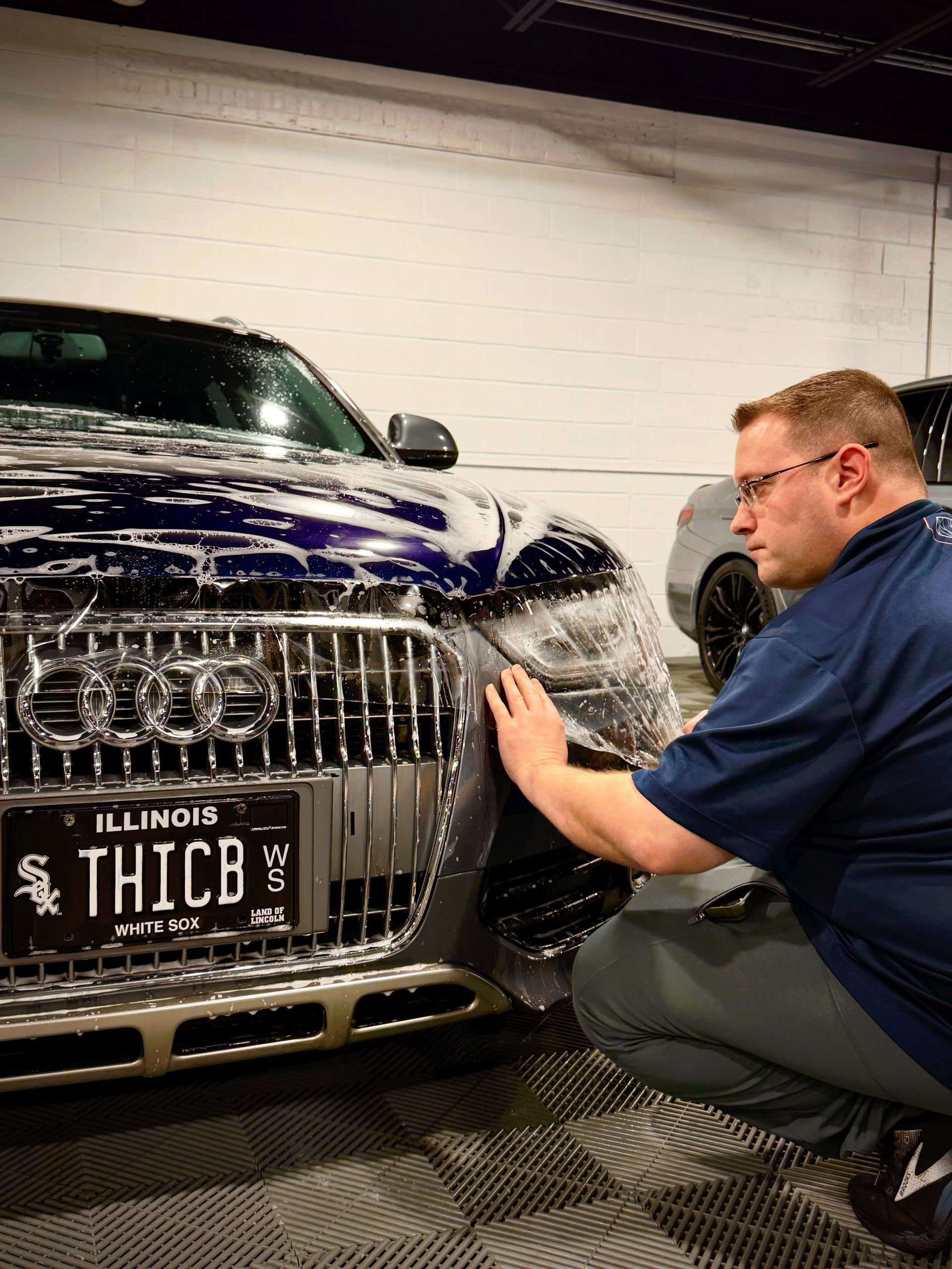 Detailing a blue Audi in a garage while a person sprays water over the grille