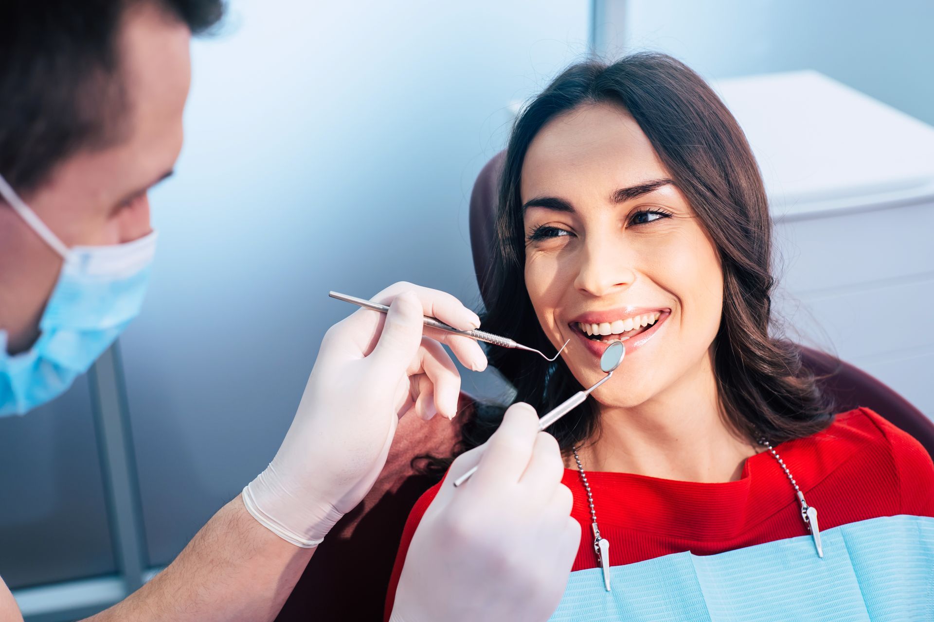 Dentist in ear loop face mask and gloves is holding dental instruments.