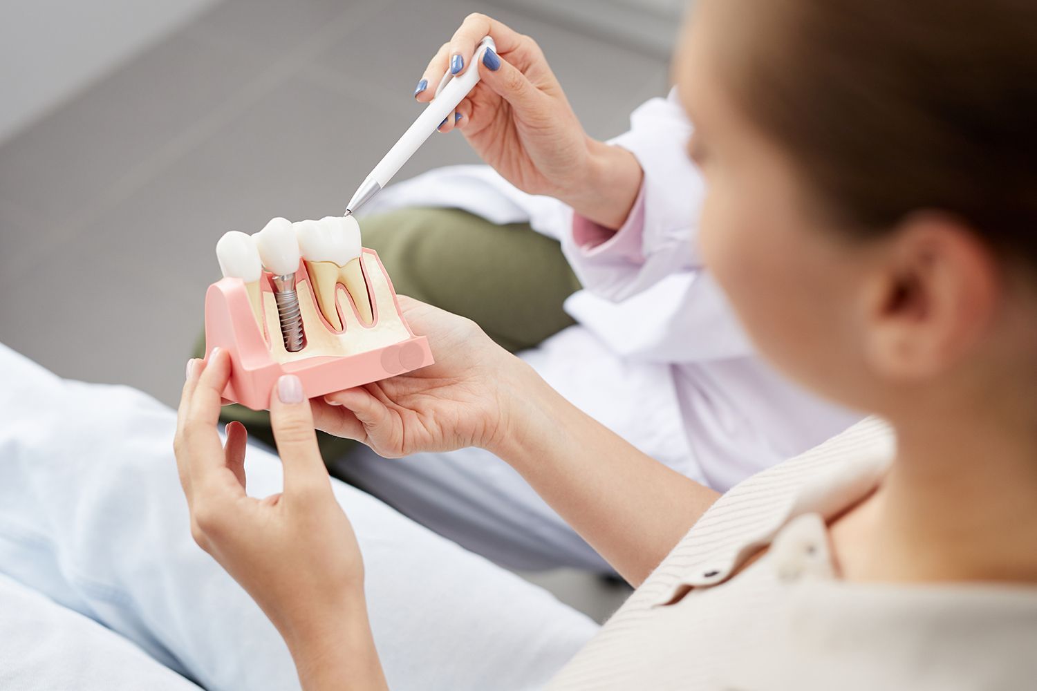A young woman holding a tooth model during a consultation in a dentist's office