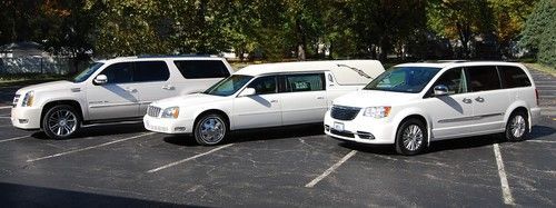 Three white minivans parked in a lot under trees