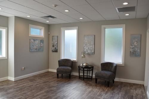 Modern waiting room with two dark chairs, small table, wall art, and frosted windows.