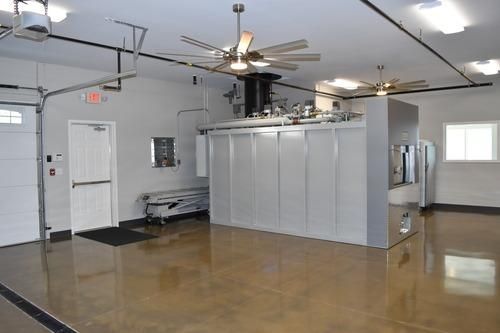 Empty industrial room with polished floor, white walls, ceiling fans, and a central metal enclosure