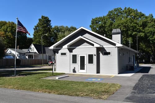 Small white building with a driveway and American flag in front, on a sunny street.