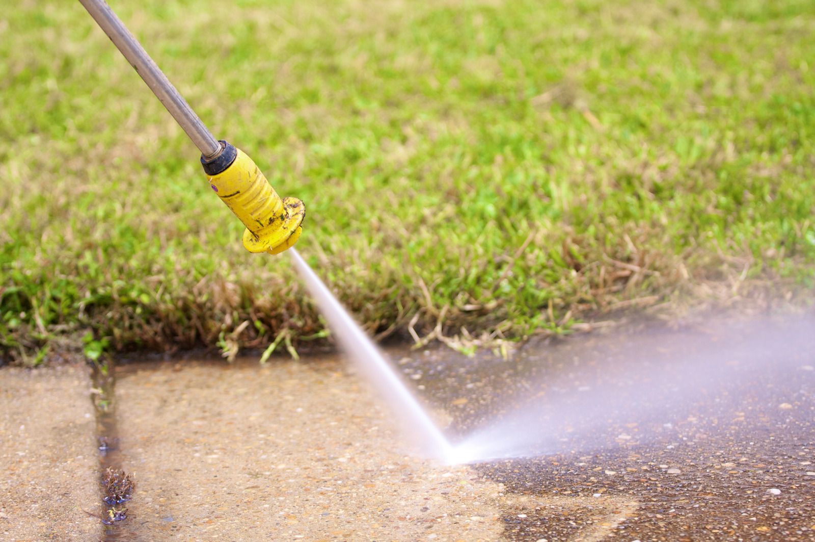 A person is using a high pressure washer to clean a sidewalk.