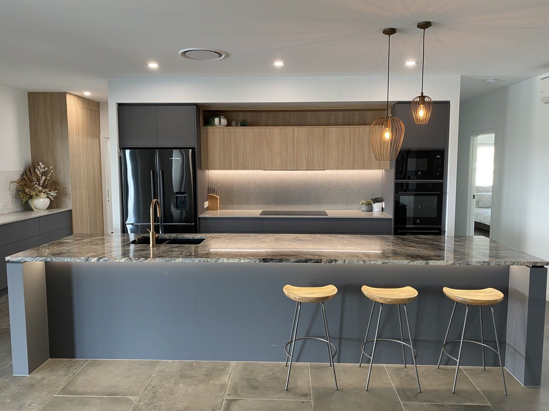 A kitchen with a large island , stools and a refrigerator.