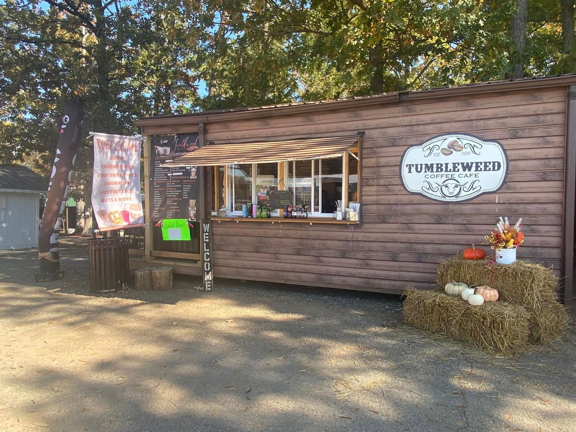 Small rustic wooden food stand in a wooded area, with a “Tumbleweed.” sign and hay bales by the entrance.