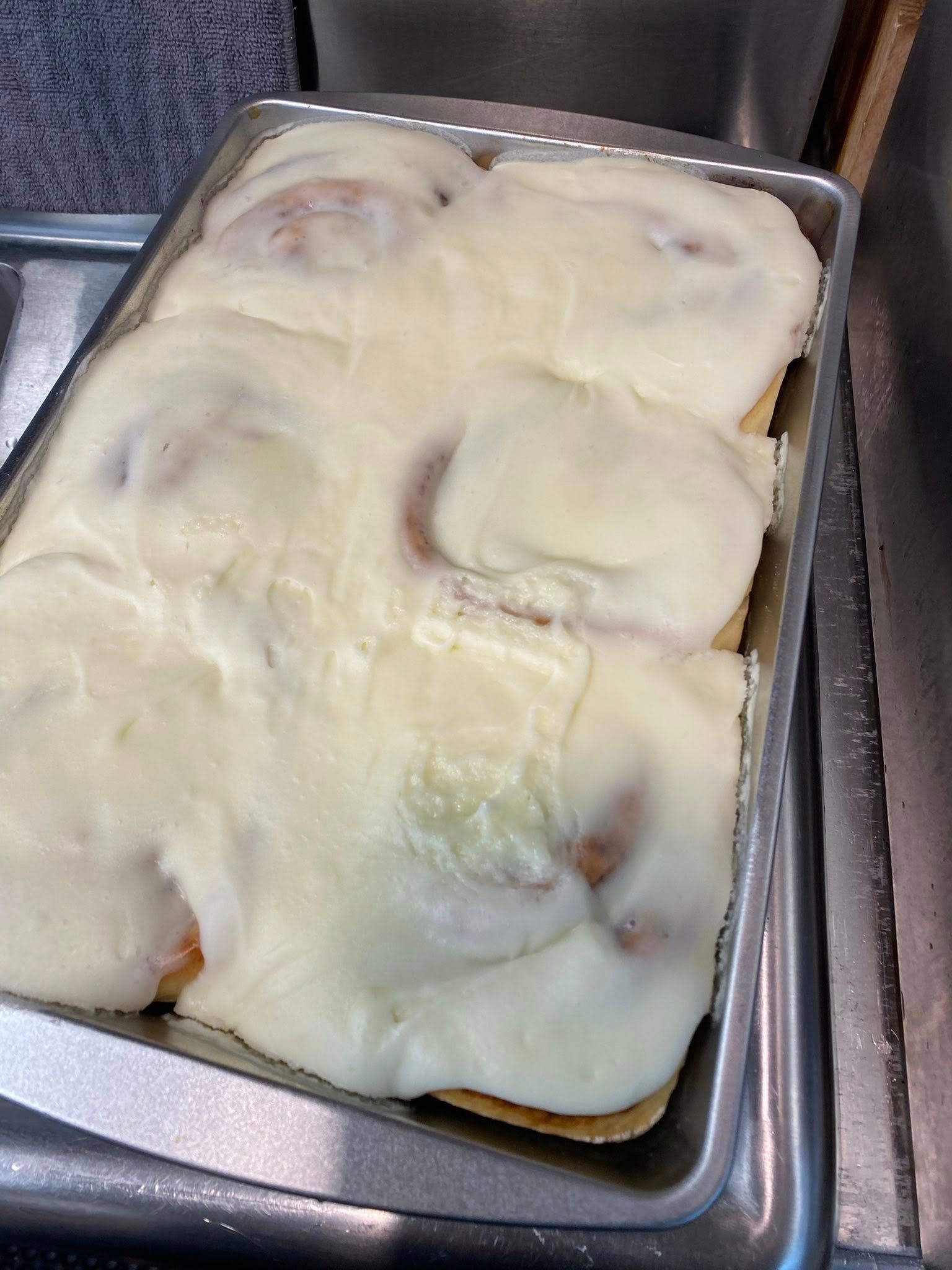 Tray of cinnamon rolls covered with smooth white icing