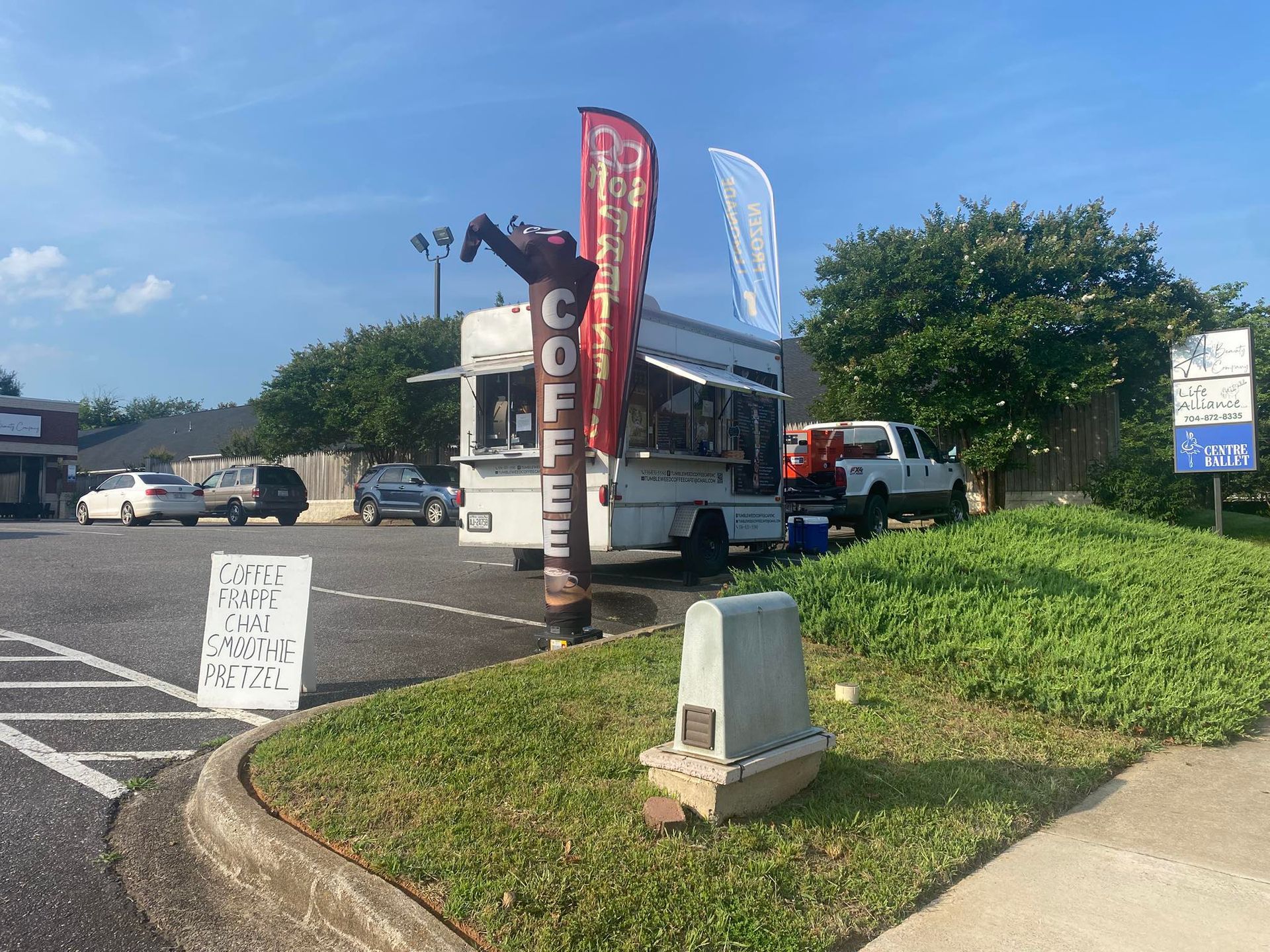 Bus parked in a lot near tall red and white flags and a grassy curb under a blue sky