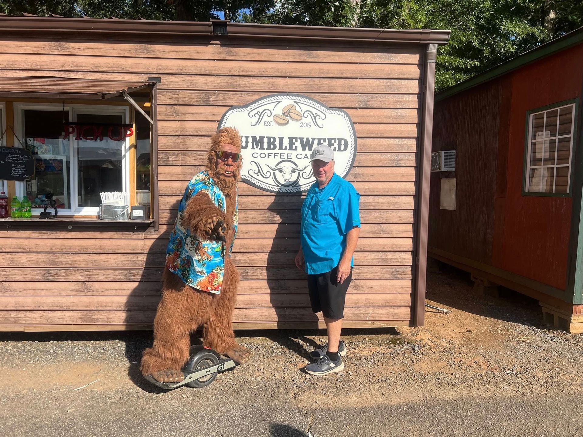 Person with a bear statue outside a wooden shop, beside a sign reading “Tumbleweed.”