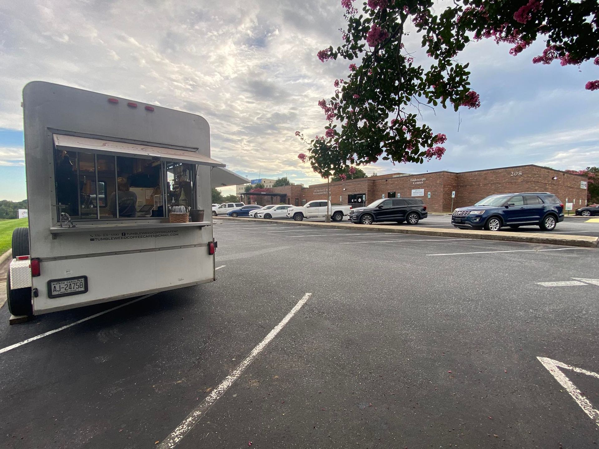 White food truck parked in a lot beside a low brick building under a cloudy sky