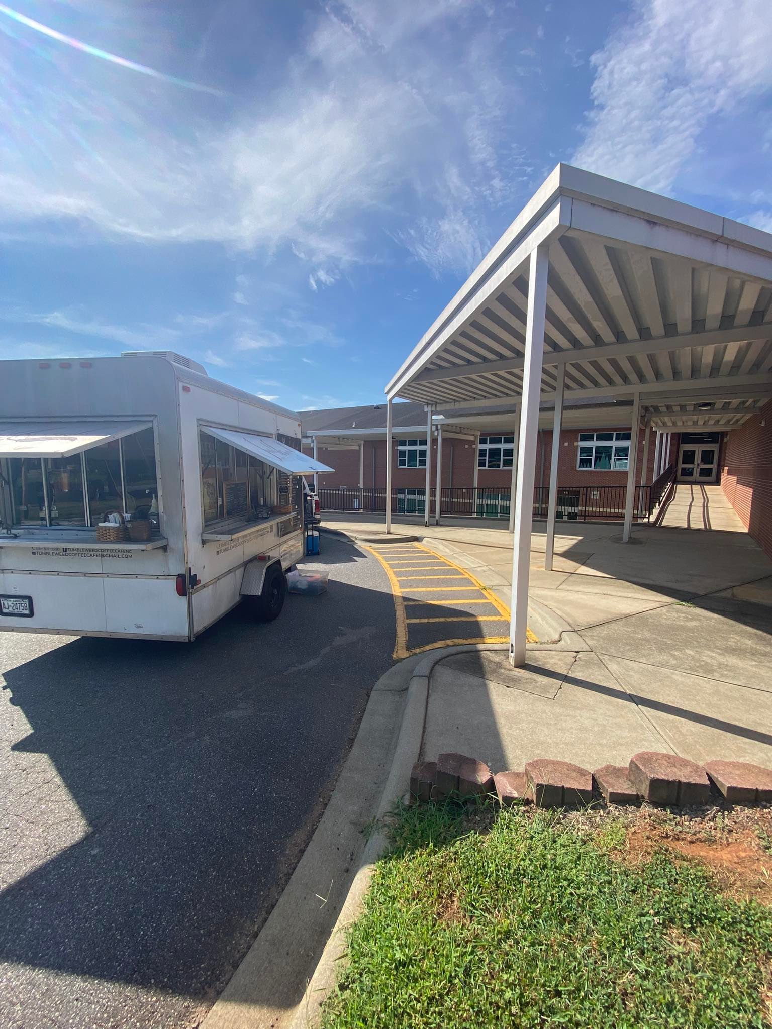 Covered walkway and parked white shuttle bus outside a brick building on a sunny day.