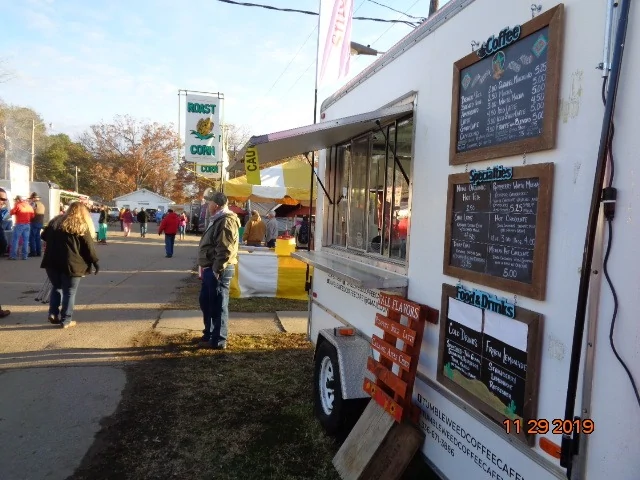 Outdoor fair scene with a white food truck, menu boards, and people walking on a sunny street