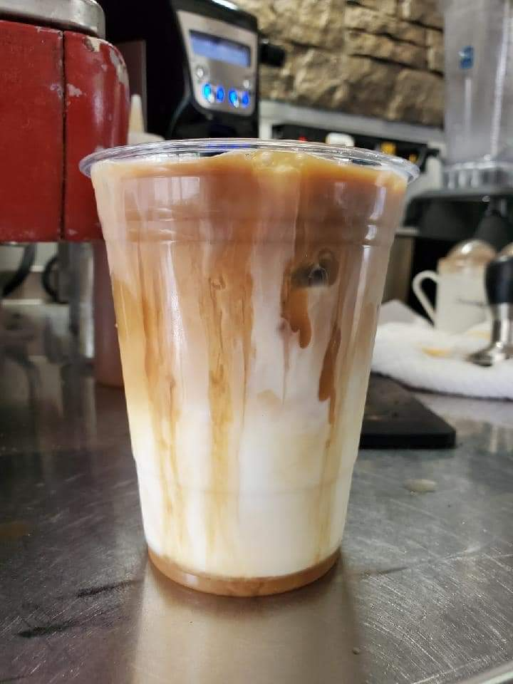 Iced coffee in a clear plastic cup with milk and caramel drizzle on a café counter