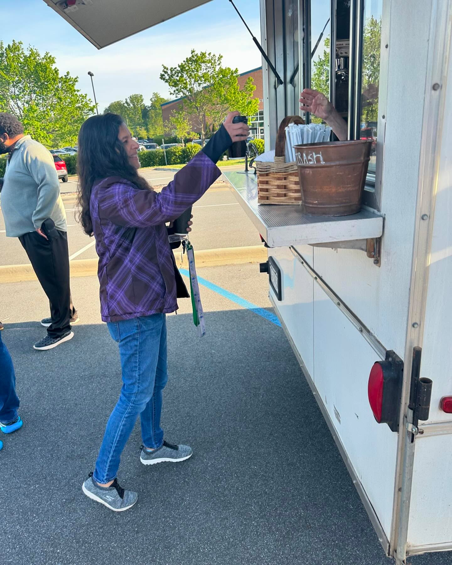 Person in purple jacket accepts an item from a vendor at a food truck window outdoors.