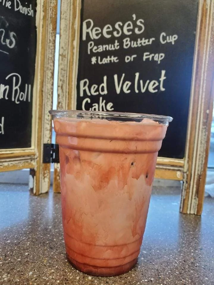 Pink blended drink in a clear plastic cup on a café counter, with a chalkboard menu behind it