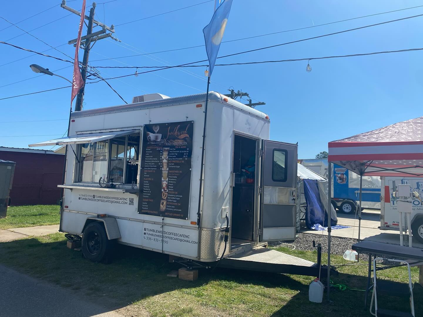 White food truck with serving window parked outdoors under a clear blue sky.