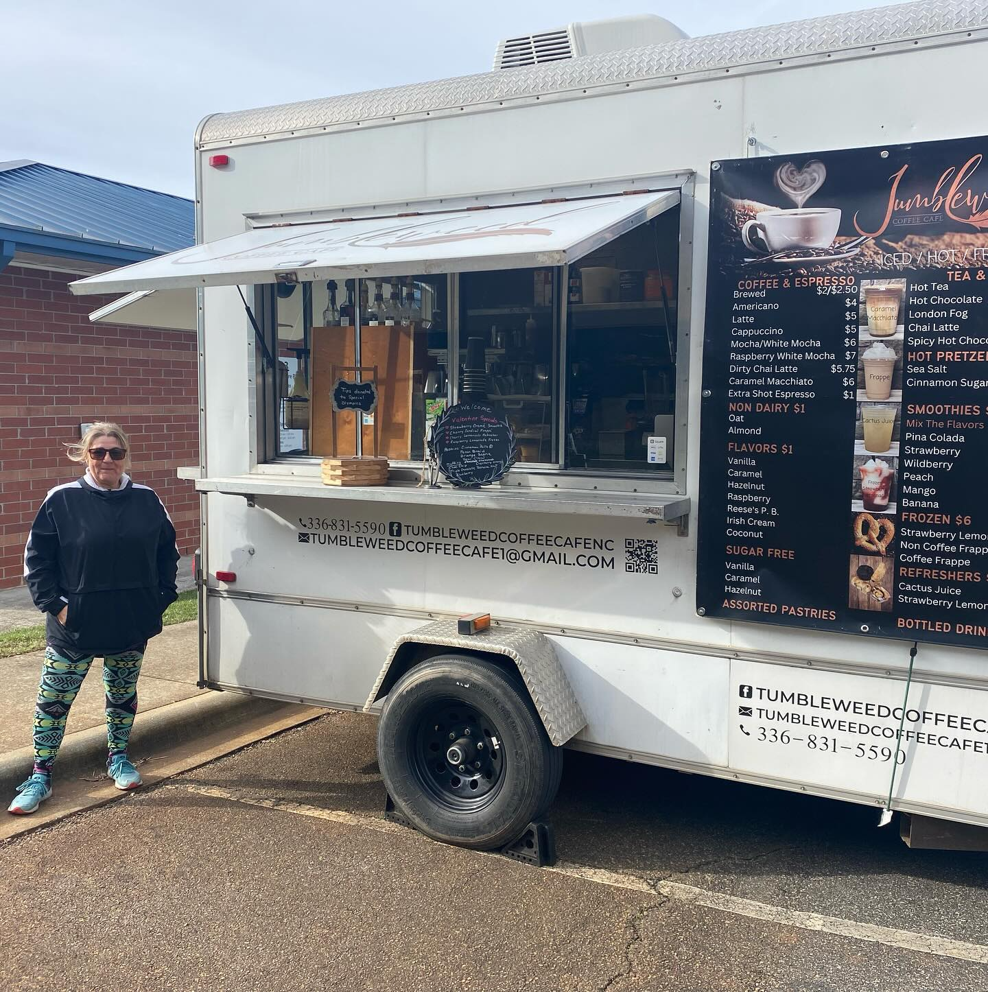 Person standing beside a white coffee truck with a menu board and awning at the curb.