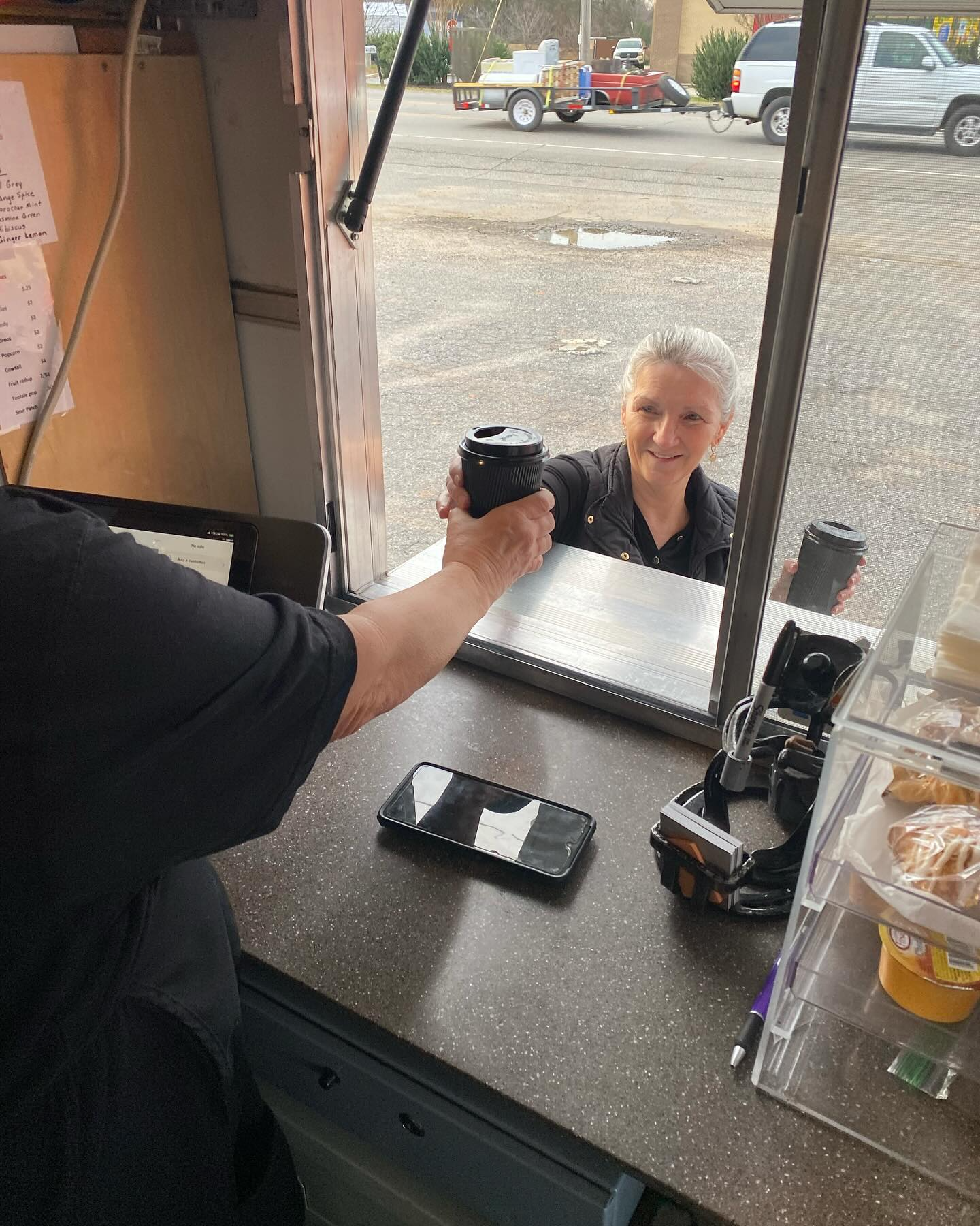 A food truck worker passes a drink to a customer at the service window.