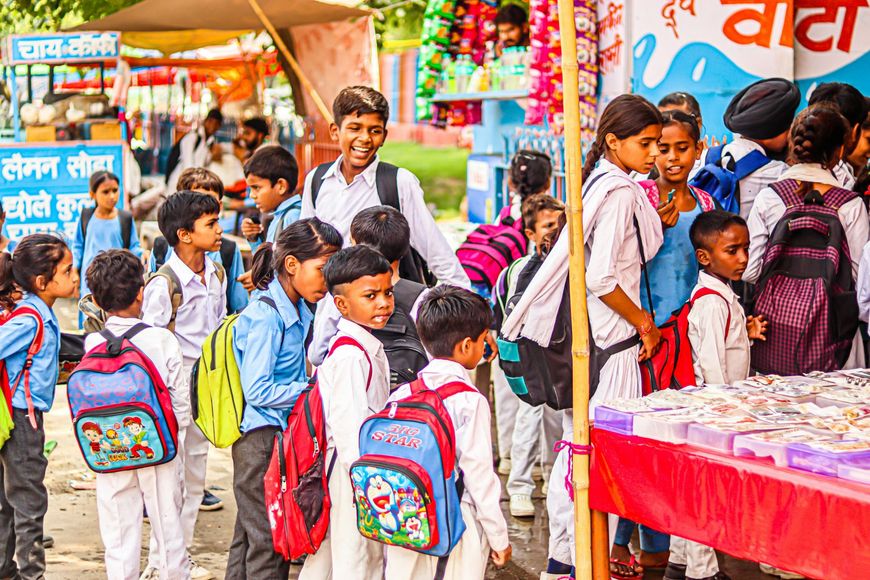 Schoolchildren with backpacks lining up at a colorful market stall or school kiosk