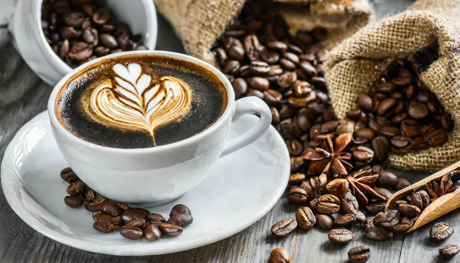 White cup of latte art on saucer, surrounded by coffee beans and burlap sack