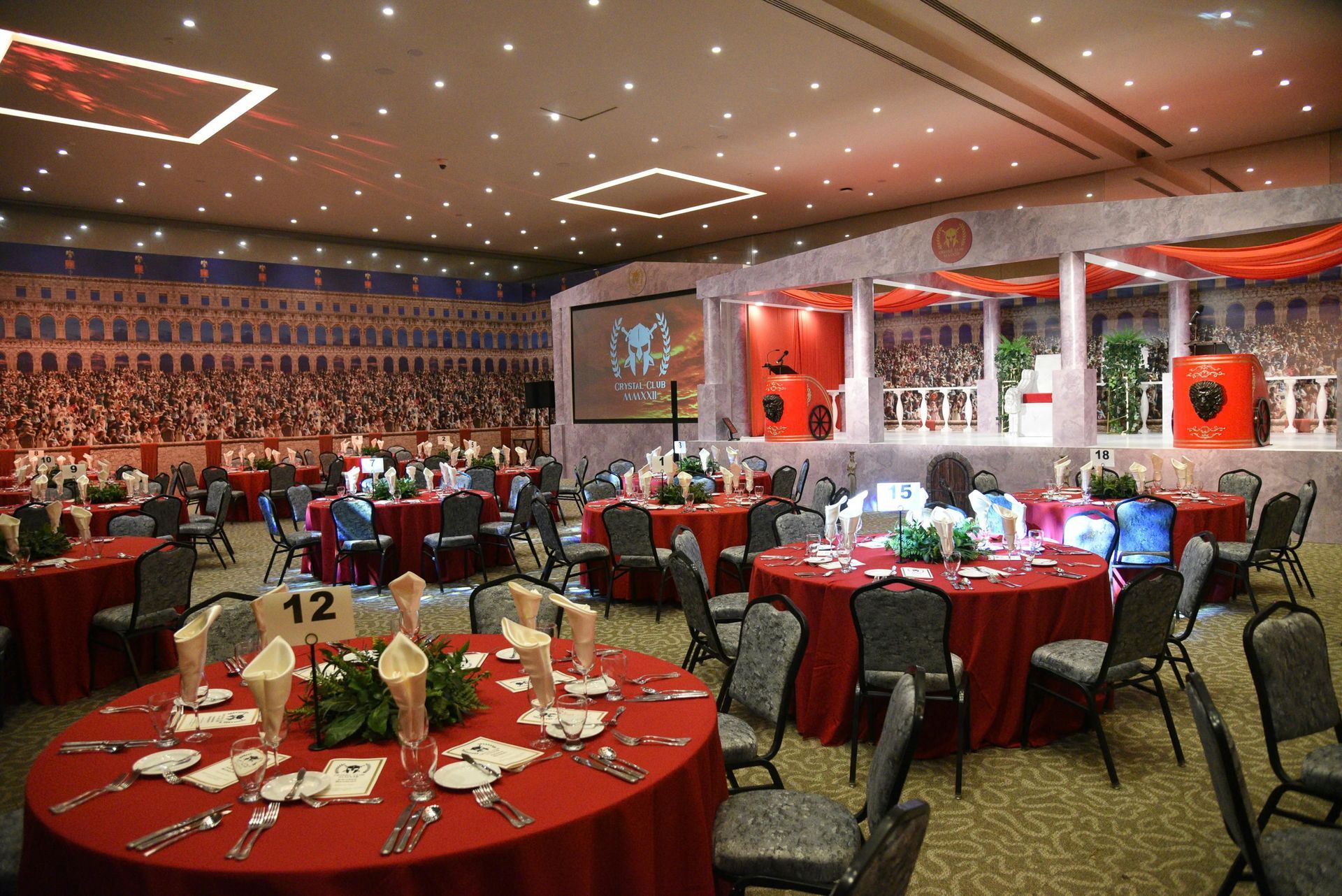 Banquet hall with round red tables set for a formal event and a stage at the front