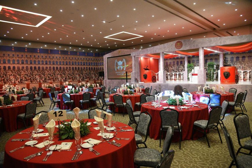 Banquet hall with round red tables set for a formal event, guests seated throughout the room.