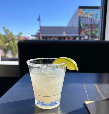 Salt-rimmed margarita with lime garnish on a table, outdoors on a sunny day.